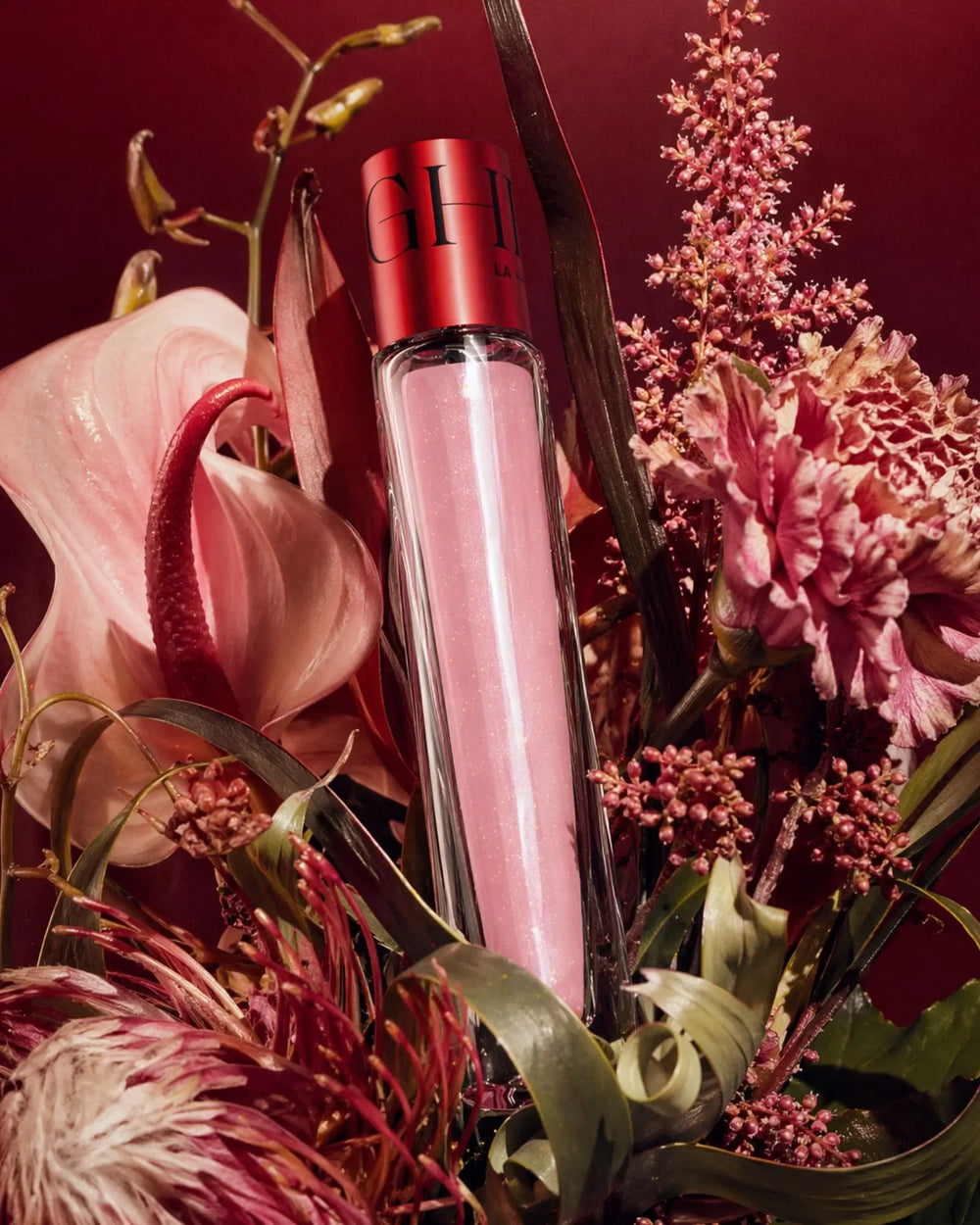 Pink perfume bottle with red cap surrounded by pink flowers on a dark red background